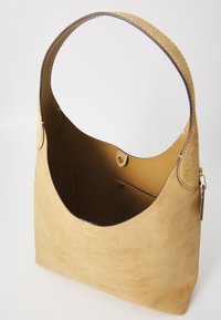 Suede hobo bag in light tan with a smooth interior. Features a rounded handle and a snap closure pocket inside. Simple, minimalist design.