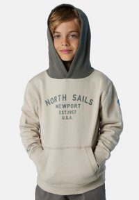 Sudadera beige con un forro de capucha gris oscuro, que presenta un diseño impreso que dice "NORTH SAILS NEWPORT EST. 1957 U.S.A.". Incluye un bolsillo frontal.