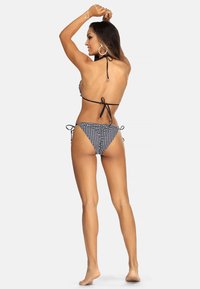 Czarny i biały bikini w kratę z dekoltem na halter i detalami wiązanymi. Góra ma falbany na brzegach, a dół ma niskie wycięcie.