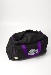 Zwarte sporttas met paarse banden, voorzien van een Lakers-logo in het wit. Gemaakt van stevig stof, met een ritssluiting en een ruime binnenkant.