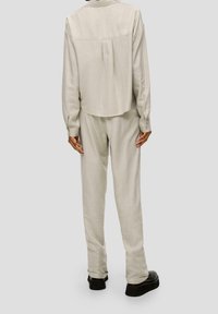 Light beige, loose-fitting shirt with a back pleat and button cuffs paired with matching trousers. Smooth texture, paired with black shoes.