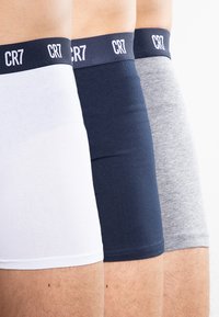 Three pairs of men's boxer shorts in white, navy, and grey, featuring a soft elastic waistband with "CR7" logo. Smooth, stretch fabric.
