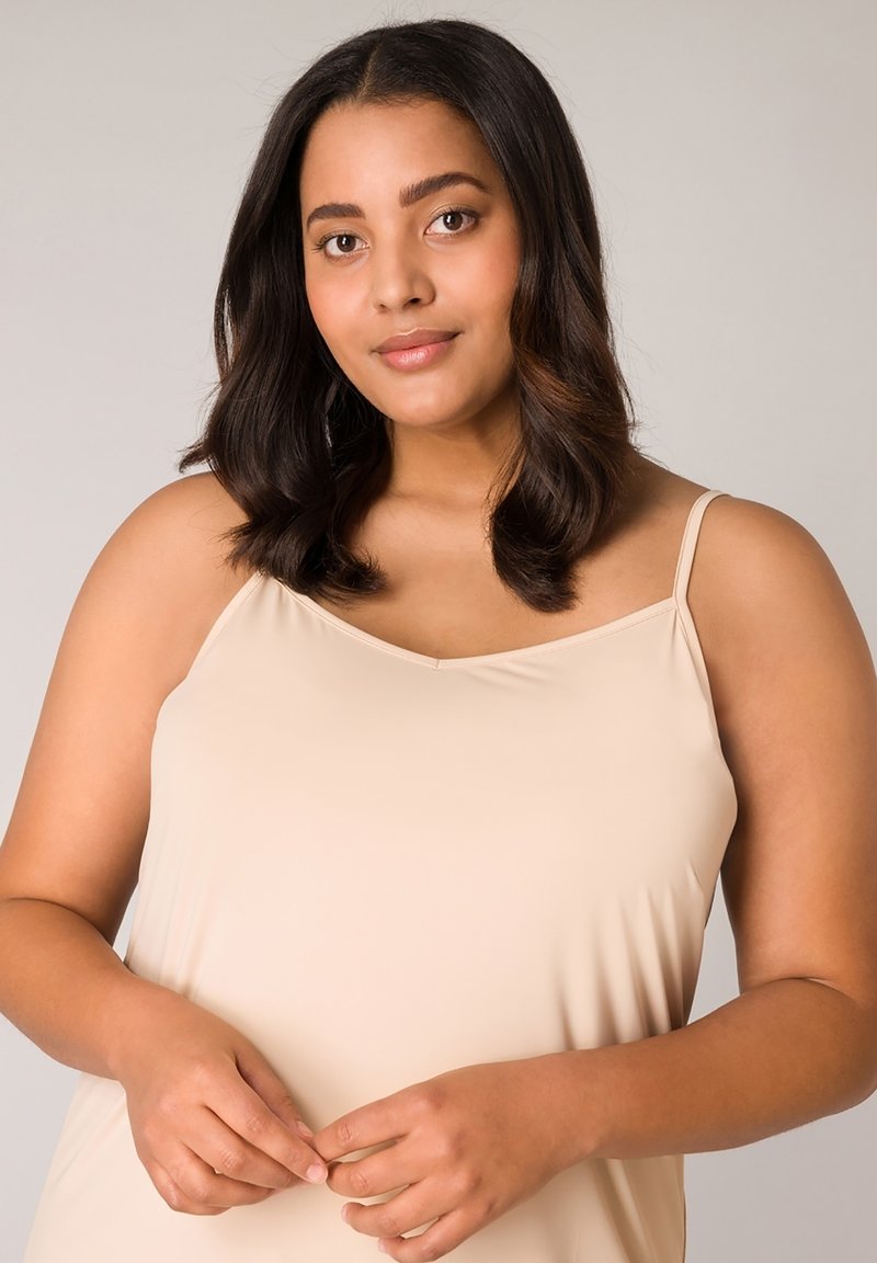 Nude, mouwloos hemd met een gladde, zachte textuur. Voorzien van dunne bandjes en een ontspannen pasvorm, waardoor een eenvoudige, elegante silhouet ontstaat.