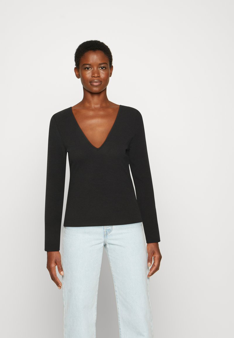 Camisola preta de mangas longas com um design de decote em V profundo, feita de um tecido suave. Combinada com jeans de perna reta azul claro.