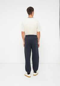 Marineblå joggebukser med elastisk midjebånd og mansjetter, med en baklomme. Kombinert med en lysefarvet t-skjorte og casual sko.