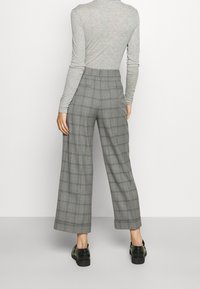 Szare spodnie w kratę z szerokimi nogawkami, gładkim materiałem i wysokim stanem. Połączone z czarnymi butami, które mają szczegóły w kratę.