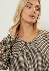 Rutig blus i kräm och marinblå, med en stor krage, knäppning fram och något rynkade ärmar med knyt detaljer.