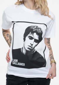 White cotton t-shirt featuring a black and white graphic of a male figure's face, with "LIAM GALLAGHER" text below in bold font.