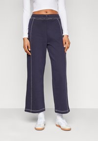 Navyblauwe wijde sweatpants van een katoenmix, met contrasterende witte stiksels en een elastische tailleband. Gecombineerd met witte sneakers.