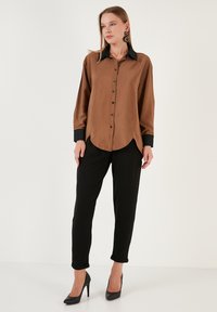 Brown satin button-up shirt with black collar and cuffs, paired with black tapered pants and black high heels. Textured fabric, fitted design.