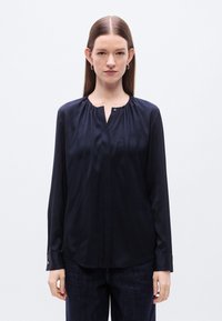 Μπλούζα μακρυμάνικη σε ναυτικό μπλε χρώμα από λείο, γυαλιστερό ύφασμα, με πτυχώσεις στον λαιμό και λεπτομέρειες μανσέτας με κουμπιά. Απλός και κομψός σχεδιασμός.