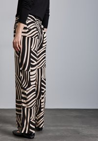 Wide-leg pants featuring a bold black and cream abstract striped pattern, with an elastic waistband and soft fabric texture.