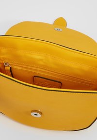 Borsa a tracolla in pelle gialla con chiusura a calamita, dotata di una tasca interna con cerniera e una texture liscia. Il bordo nero accentua il design.