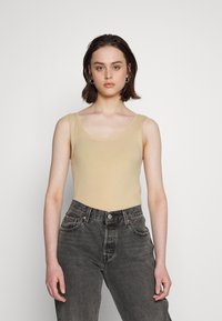 Camisola justa beige com decote redondo, combinada com jeans escuros de cintura alta. Tecido suave, sem padrões ou adornos visíveis.