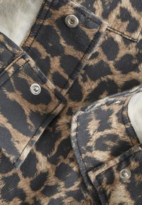 Látka s leopardím vzorem v odstínech hnědé a černé, s kovovými patentkami a měkkou texturou, s překrývajícími se klopami, které ukazují detaily šití.
