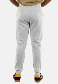 Gray sweatpants with an elastic waistband, tapered legs, and side pockets. Paired with black and orange sneakers.