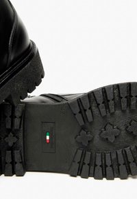 Schwarze Lederstiefel mit einem hochglänzenden Obermaterial, strapazierfähiger Gummisohle mit einem Profilmuster und einem sichtbaren Reißverschluss an der Seite.