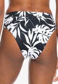 Černé bikiny s nízkým pasem, zdobené bílým tropickým vzorem listů, vyrobené z hladké elastické tkaniny pro pohodlí.