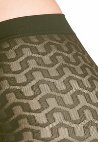 Collants à motifs olive avec un design en zigzag texturé, dotés d'une taille lisse. Le tissu présente une qualité semi-transparente.