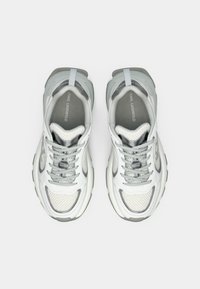 Fehér és szürke hálós sportcipők texturált mintával, lekerekített formával, megerősített orr-résszel, valamint logó díszítésekkel a nyelvnél és az oldalon.