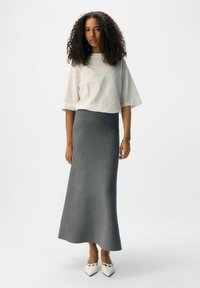 Gray wool maxi skirt with a fitted waistband and flowing silhouette, paired with a white loose-fitting cotton top. White pointed shoes.
