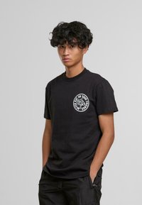 T-shirt en coton noir à manches courtes, avec un imprimé graphique circulaire blanc sur la poitrine et un col rond.