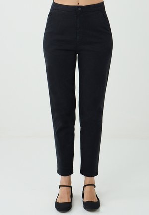 Pantalons noirs taille haute associés à des ballerines noires, dotés d'une simple fermeture à bouton et à zip, présentés sur un fond neutre.
