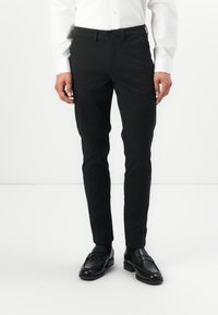 Black slim-fit trousers made of cotton blend fabric, featuring a smooth texture and front pockets, worn with black loafers and a white shirt.