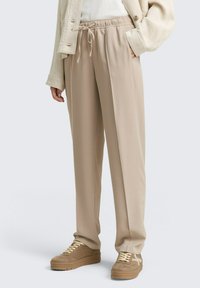 Pantalones ligeros color beige con cintura el�ástica y cordón. Tienen un corte relajado y perneras rectas, combinados con zapatillas beige.
