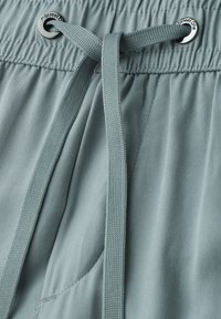 Lichtblauwe stoffen broek met elastische taille en platte trekkoord die door metalen oogjes met het label "Street One" is geregen.