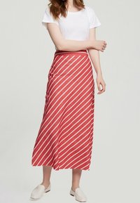 Jupe maxi à rayures rouges et blanches avec taille haute, fabriquée en tissu léger. Complétée par un simple t-shirt blanc et des chaussures légères.