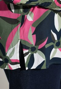 Tumma sininen kukkaita sisältävä pusero, jossa on vaaleanpunaisia, valkoisia ja vihreitä kukkia. Kankaassa on pehmeä tekstuuri, ja hemissä on sivurei'itys lisäämään muotoiluedellytyksiä.