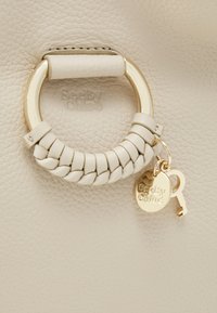 Biała skórzana torebka z plecionym uchwytem, złotymi elementami i zawieszką w kształcie klucza. Na powierzchni widnieje wytłoczone logo "See by Chloé".