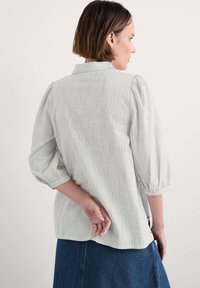 Blusa a rayas verde claro con cuello y mangas abullonadas. Tejido suave, llega hasta la cadera, presenta un corte relajado y un detalle en el yugo trasero.