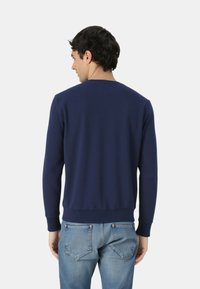 Felpa blu navy con maniche lunghe, scollo rotondo, polsini e orlo a costine. Indossata con jeans azzurri, presenta un design semplice e una vestibilità comoda.