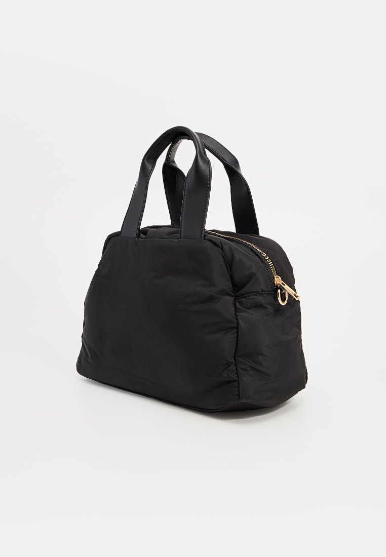 Czarna torba nylonowa z krótkimi skórzanymi uchwytami, z złotym suwakiem i lekko puszystym fasonem. Kompaktowy kształt, bez widocznych wzorów.