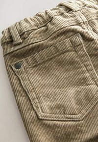 Pantalons en velours côtelé beige avec une texture côtelée, une taille élastique et une poche arrière avec un détail de rivet en métal.