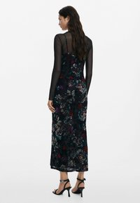 Černé květinové šaty s texturovaným vzorem, dlouhými průhlednými rukávy, přiléhavým střihem a délkou pod kolena. Černé sandály na vysokém podpatku.