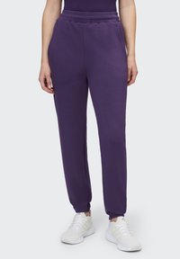 Lila Jogginghose mit elastischem Bund und Bündchen an den Knöcheln, mit glatter Textur und Seitentaschen, kombiniert mit weißen Sportschuhen.