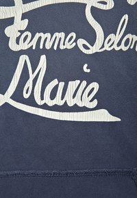 Sudadera azul marino con impresión texturizada blanca que presenta el texto "Femme Selon Marie". La tela parece suave con una textura lisa.