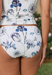 Blommig badkläder med vit bakgrund och blåa och lila blommönster, slät tyg, medelhög skärning och kontrasterande kanter.
