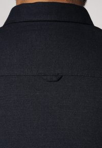 Marineblauwe shirt met een klassieke kraag, een soepele textuur en een klein lusdetail aan de achterkant, met subtiele stiksels.
