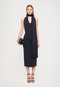 Rochie tricotată navy cu decolteu adânc în V, design halter și un fular lung cu franjuri. Accesorii cu o geantă mică neagră și sandale negre cu barete.