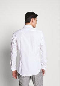 Witte blouse met lange mouwen, klassieke kraag, getailleerd ontwerp en knoopaccenten op de manchetten, gecombineerd met lichtgrijze geruite broek.