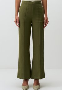 Pantalons larges vert olive en lin, avec une taille haute, des lignes épurées et une texture lisse, associés à des escarpins à bout pointu.