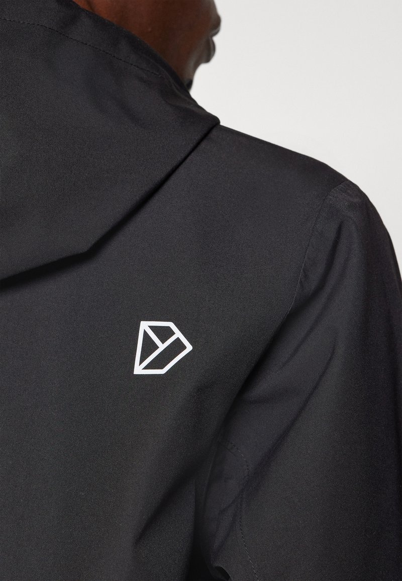 Schwarze Jacke mit Kapuze, aus glattem Material und einem weißen geometrischen Logo auf der Rückseite. Minimalistisches Design, keine zusätzlichen Muster oder Akzente.