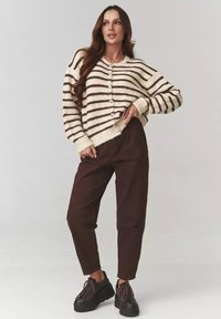 Kardigan w paski w kolorze kremowym i brązowym z guzikami, noszony na brązowych spodniach z wysokim stanem oraz czarnych butach na platformie z sznurówkami. Miękki, strukturalny dżersej.