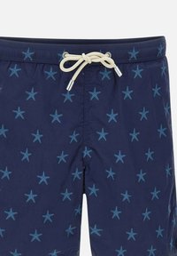 Bañador azul marino con patrón de estrellas de mar; hecho de tela ligera. Presenta una cintura con cordón y aglets de metal.