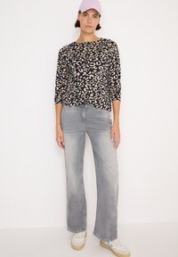 Top blu navy con stampa leopardo crema, maniche a tre quarti; jeans grigi svasati con una texture sbiadita; scarpe da ginnastica chiare con accenti multicolori.