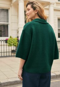 Green oversized knit sweater with a ribbed collar and short sleeves, textured fabric, paired with dark blue wide-leg pants.